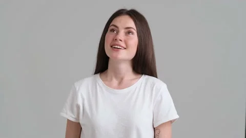 A dreaming woman wearing basic T-shirt is standing isolated over grey background Stock Footage 154947388