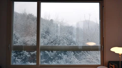 Dreamy winter snowfall view through big window from warm indoor room Stock Footage 328136465
