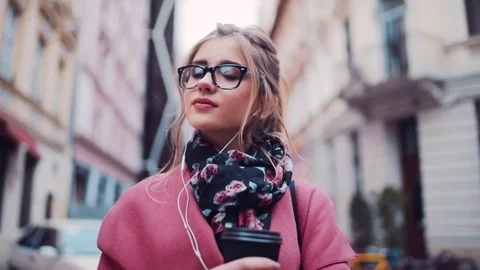 Dreamy young girl stands in the city street with cup of coffee, listening music Stock Footage