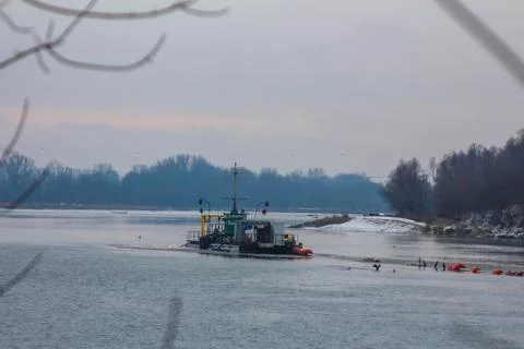 Dredging boat operates in cold river during winter day near snowy banks Stock Photos