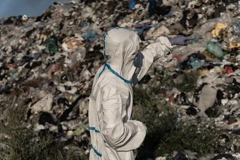 Dressed in a protective suit, a worker inspects a vast landfill, observing .. Stock Photos