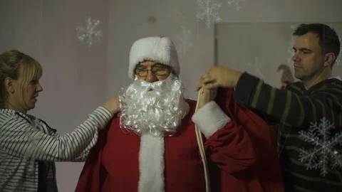 Dressing santa claus, preparing for the new year, christmas tree, funny scene. Stock Footage 99628347