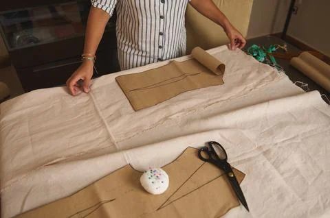 Dressmaker arranges brown paper patterns on light linen fabric with scissors, Stock Photos