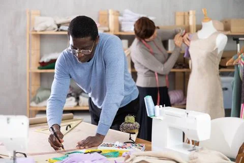 Dressmaker sketching sewing pattern while colleague adjusting dress on mannequin Stock Photos