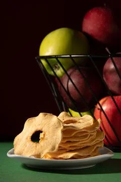 Dried apples on a white plate. Behind is a basket of apples. Studio photo on  Stock Photos