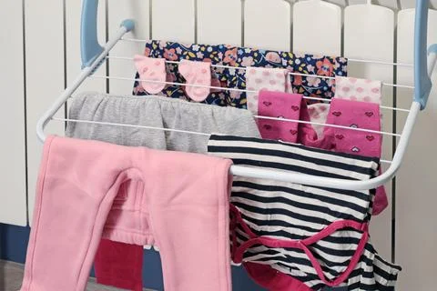 Dried clothes on mini coat rack near radiator in room. Cleanliness and children Stock Photos