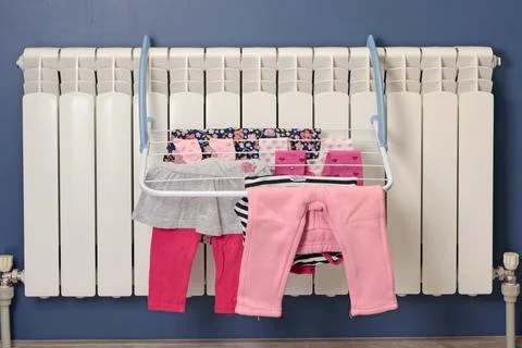 Dried clothes on mini coat rack near radiator in room. Cleanliness and children Stock Photos