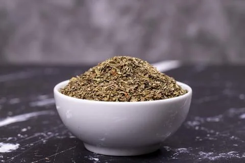 Dried crushed basil on dark background. Dried ground basil powder spices in c Stock Photos