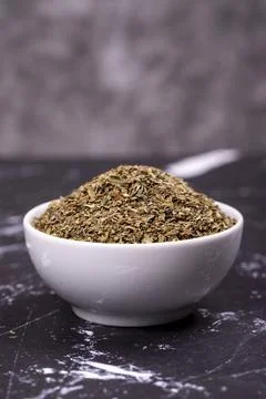 Dried crushed basil on dark background. Dried ground basil powder spices in c Stock Photos