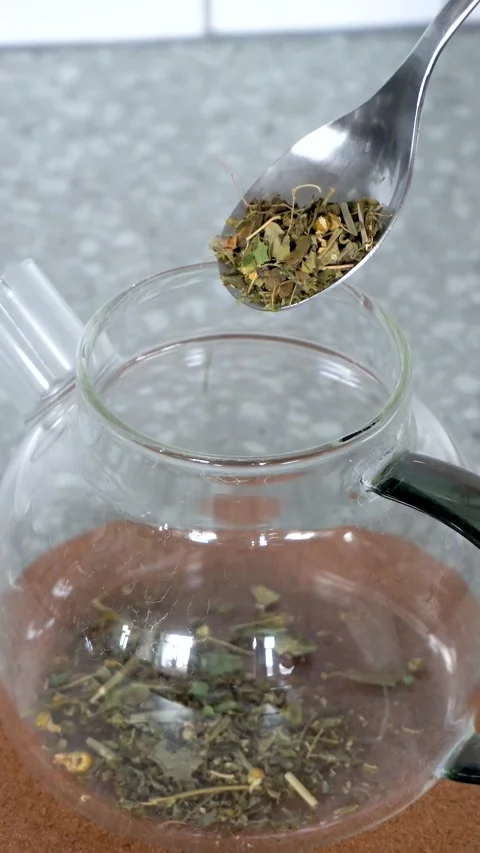 Dried herbal tea added with spoon into transparent glass teapot Stock Footage 335776116