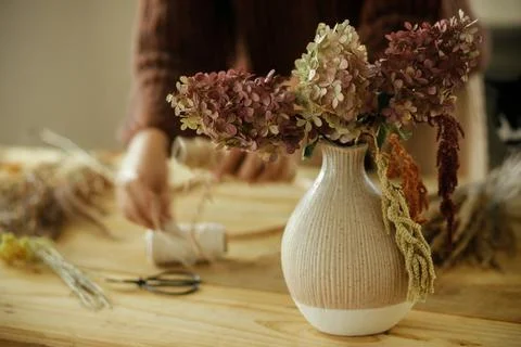 Dried hydrangea flowers in vase on background of woman arranging dried gras.. Stock Photos