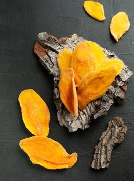 Dried mango slices. On the bark of a tree. View from above. Dark background. Stock Photos