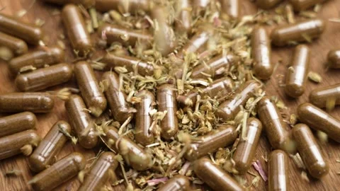 Dried medicinal yarrow herbs falling onto herbal supplement capsules Stock Footage 289748201