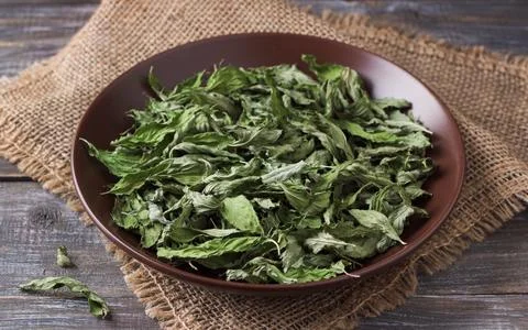 Dried mint leaves in a brown ceramic bowl on burlap on a wooden table, close  Stock-Fotos