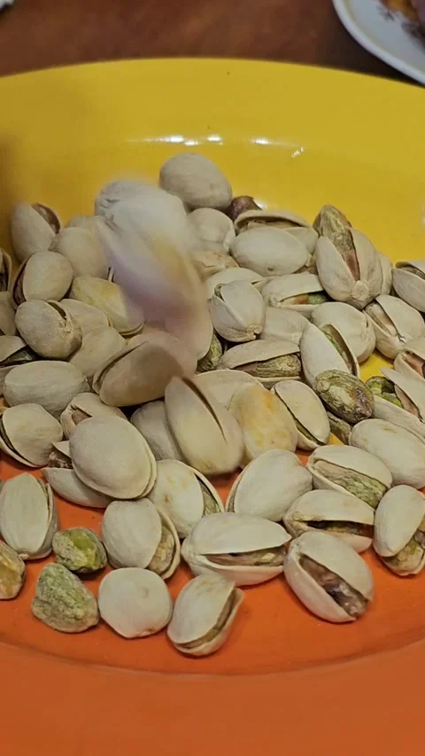 Dried pistachios with cracked shells and green kernels falling onto a plate Stock Footage 305992082