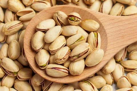 Dried pistachios with green kernels in a rustic wooden spoon close up. Delici Stock Photos