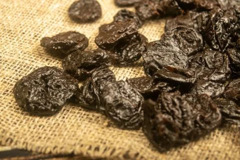 Dried prunes in bulk on burlap with a rough texture. Close up. Stock Photos