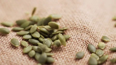 Dried pumpkin seeds falling onto a rustic burlap Stock Footage 336548735