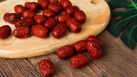 Dried red dates - jujubes - scattered on a light cutting board and dark rustic Stock Footage 331572872
