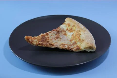 Dried slice of pizza on a black table on a blue background. Food concept. Stock Photos