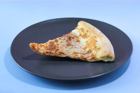 Dried slice of pizza on a black table on a blue background. Food concept. Stock Photos