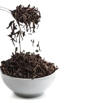 Dried tea pour from the spoon in ceramic cup over white background. Stock Photos