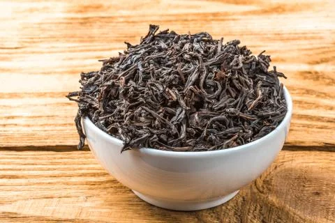 Dried tea is poured into a ceramic cup on a wooden plank table. Stock Photos