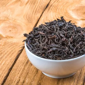 Dried tea is poured into a ceramic cup on a wooden plank table. Stock Photos