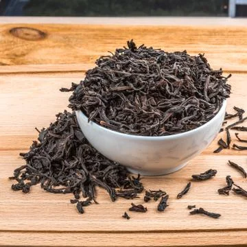 Dried tea is poured into a ceramic cup on a wooden plank table. Stock Photos