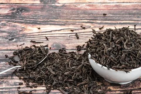 Dried tea is poured into a ceramic cup on a wooden plank table. Stock Photos