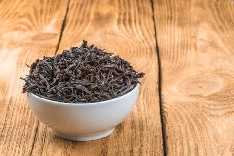 Dried tea is poured into a ceramic cup on a wooden plank table. Stock Photos