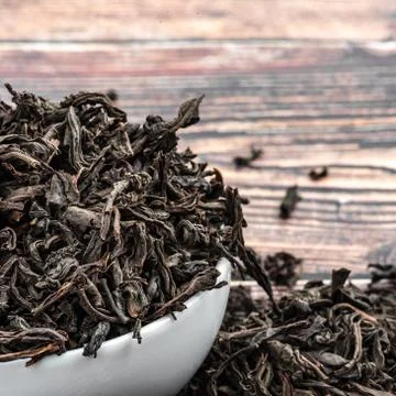 Dried tea is poured into a ceramic cup on a wooden plank table. Stock Photos
