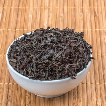 Dried tea is poured into a ceramic cup on a bamboo mat. Stock Photos