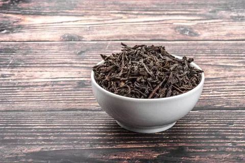 Dried tea is poured into a ceramic cup on a wooden plank table. Stock Photos
