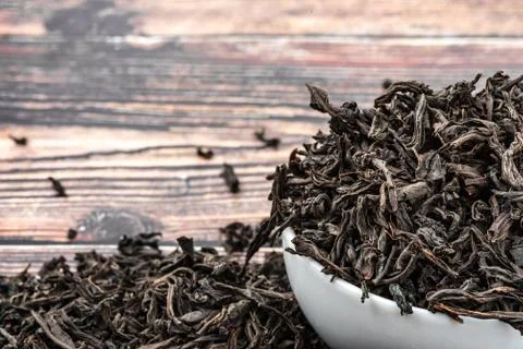 Dried tea is poured into a ceramic cup on a wooden plank table. Stock Photos