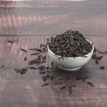 Dried tea is poured into a ceramic cup on a wooden plank table. Stock Photos
