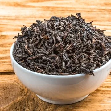 Dried tea is poured into a ceramic cup on a wooden plank table. Stock Photos