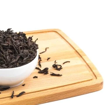 Dried tea is poured into a ceramic cup on a wooden board on a white backgroun Stock Photos