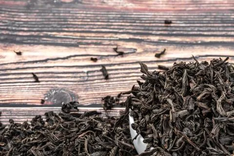 Dried tea is poured into a ceramic cup on a wooden plank table. Stock Photos