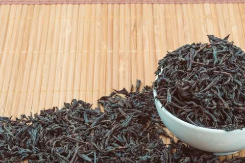 Dried tea is poured into a ceramic cup on a bamboo mat. Stock Photos