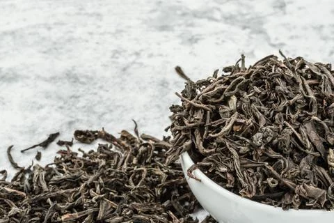 Dried tea is poured into a white ceramic cup on a marble table. Stock Photos