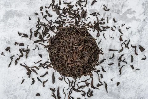 Dried tea is poured into a white ceramic cup on a marble table. View from abo Stock Photos