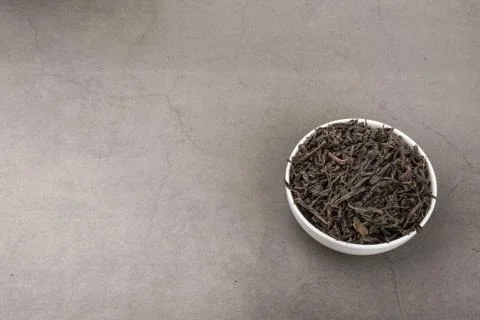 Dried tea is poured into a white ceramic cup on a gray textured background. Stock Photos
