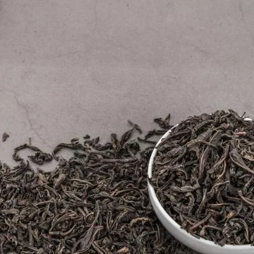 Dried tea is poured into a white ceramic cup on a gray textured background. Stock Photos