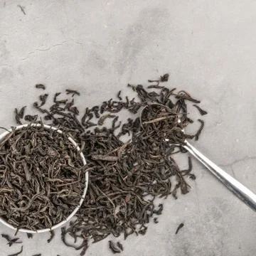Dried tea in a white ceramic cup with a spoon on a gray textured background.  Stock Photos