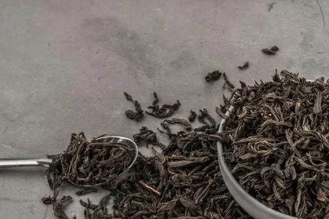 Dried tea in a white ceramic cup with a spoon on a gray textured background. Stock Photos