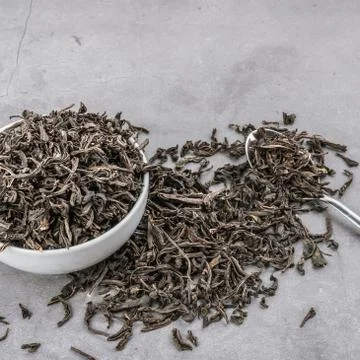 Dried tea in a white ceramic cup with a spoon on a gray textured background. Stock Photos