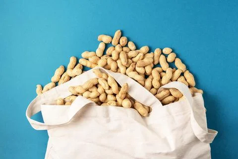 Dried uncleaned peanuts from a fabric bag on a blue background. 스톡 사진