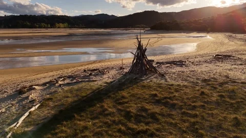 Driftwood firepit structure on vast tidal sandflat with shallow reflective Stock Footage 336849611