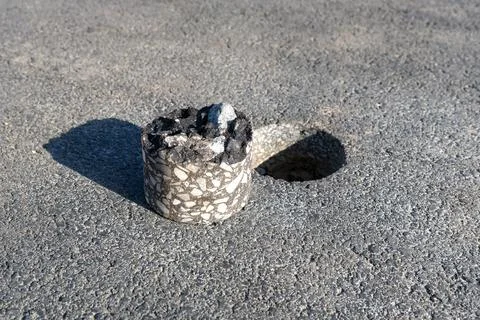 Drilled asphalt core sample lying on road surface near inspection hole during Stock Photos
